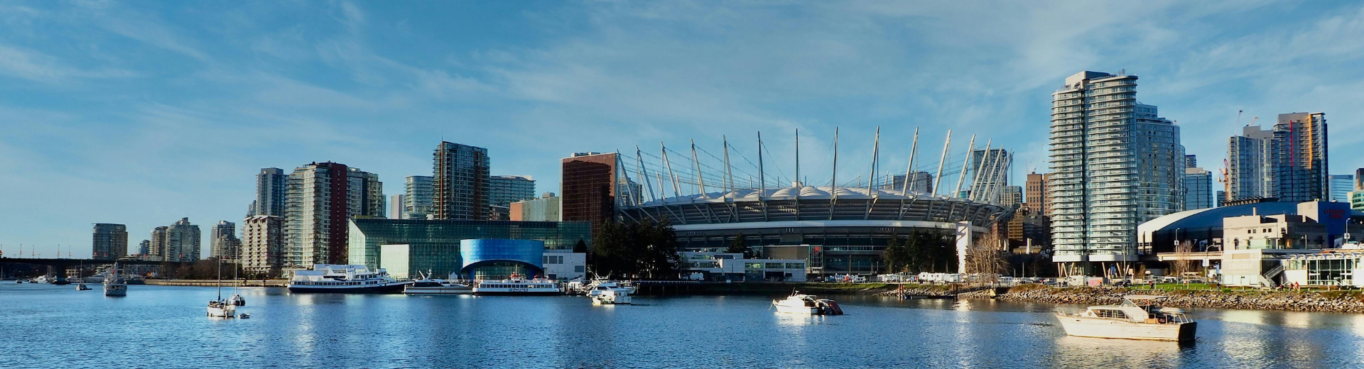 Vancouver, British Columbia coastal view, showing BC Place and high-rise buildings, surrounded by blue skies and calm sea water. 