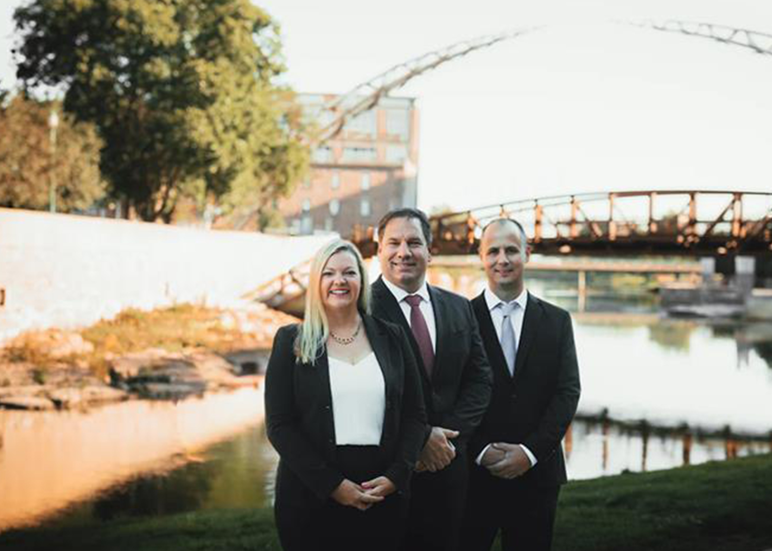 Two men and one woman in professional dress outdoor with bridge in background