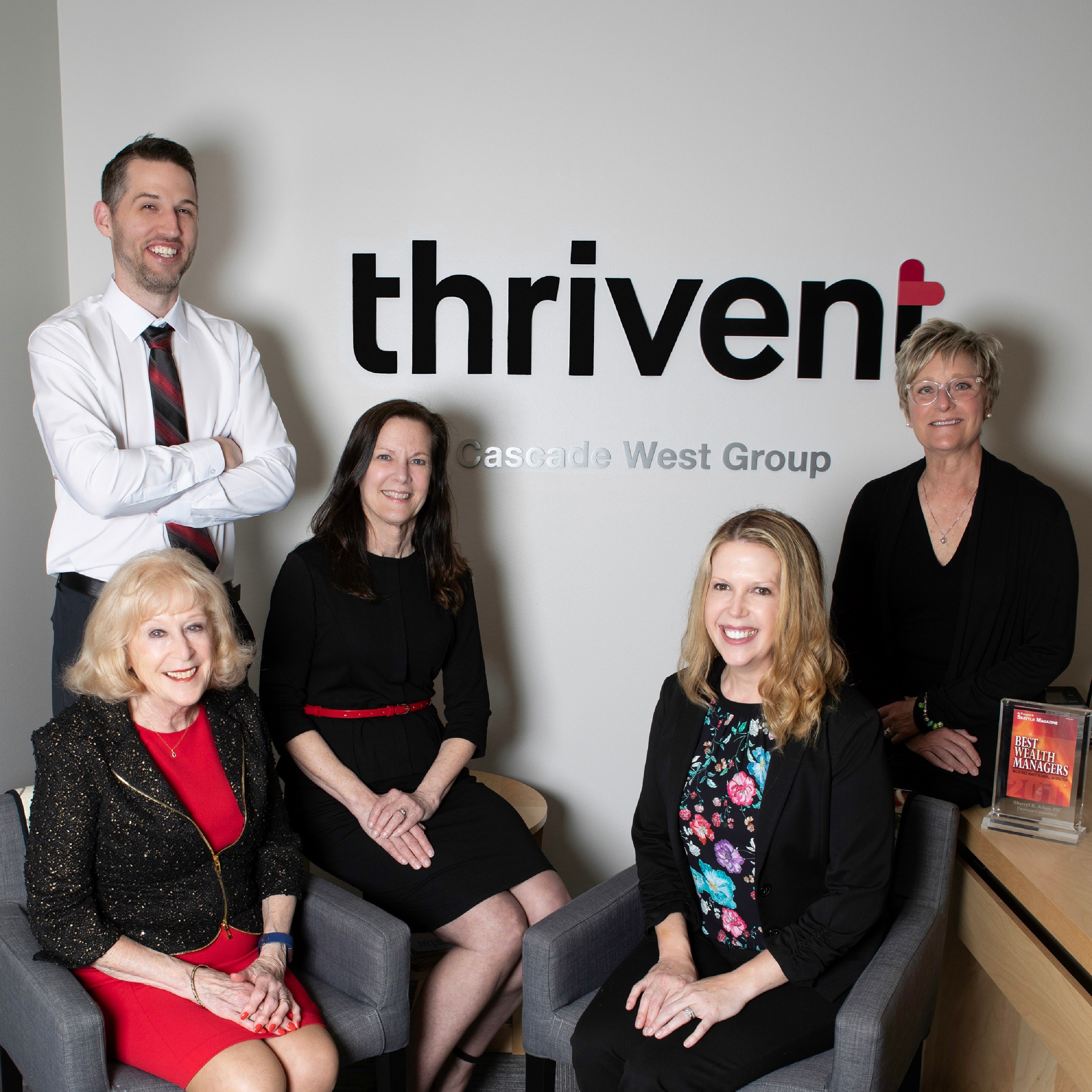 Four women and one man in professional dress, sitting in an office setting looking at the camera