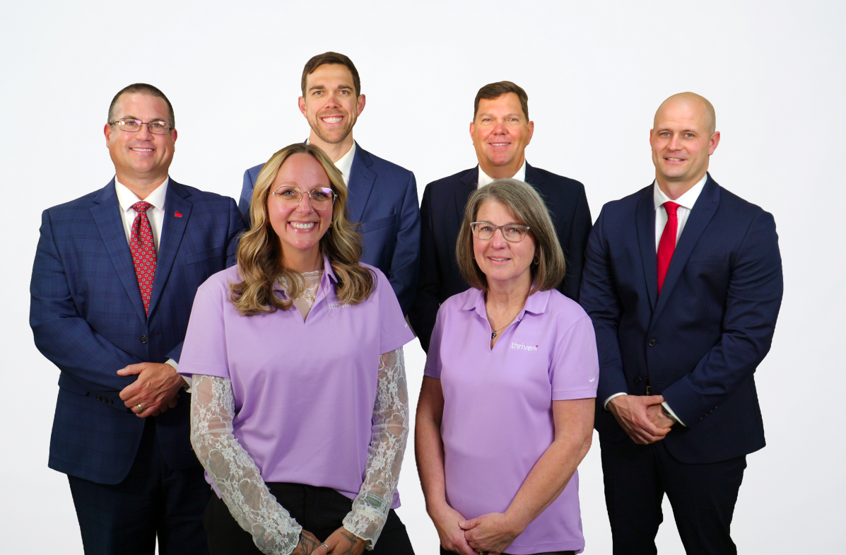 Four men and two women in professional dress standing in from of Thrivent sign smiling at the camera