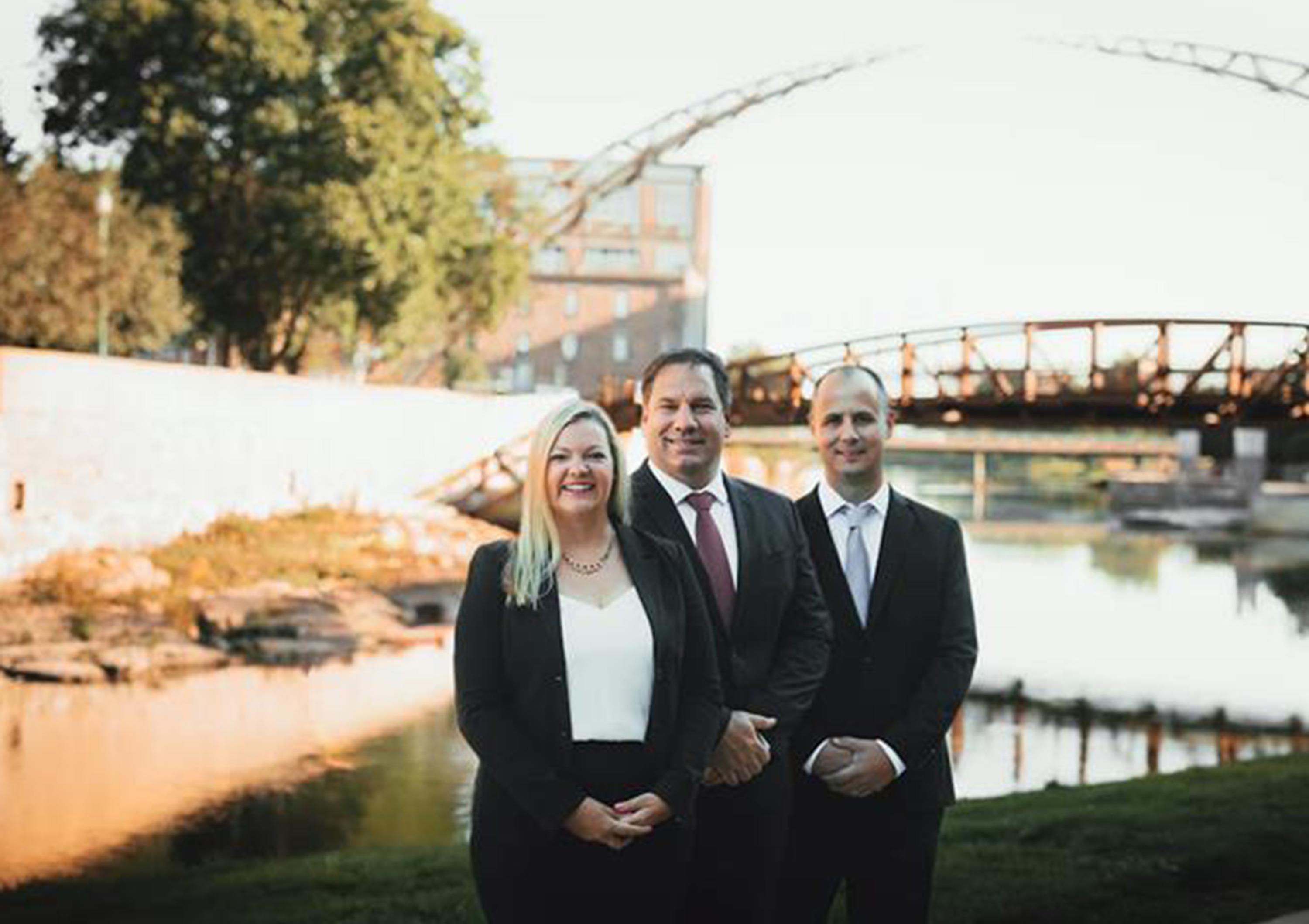 Two men and one woman in professional dress outdoor with bridge in background